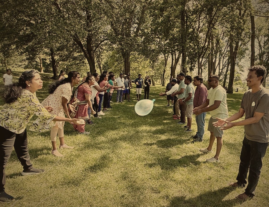 Church families playing a water balloon toss in two lines under the trees at the summer picnic